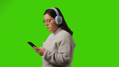 Mujer-Joven-Con-Auriculares-Inalámbricos-Transmitiendo-Música-Desde-Un-Teléfono-Móvil-Contra-La-Pantalla-Verde-Del-Estudio-1